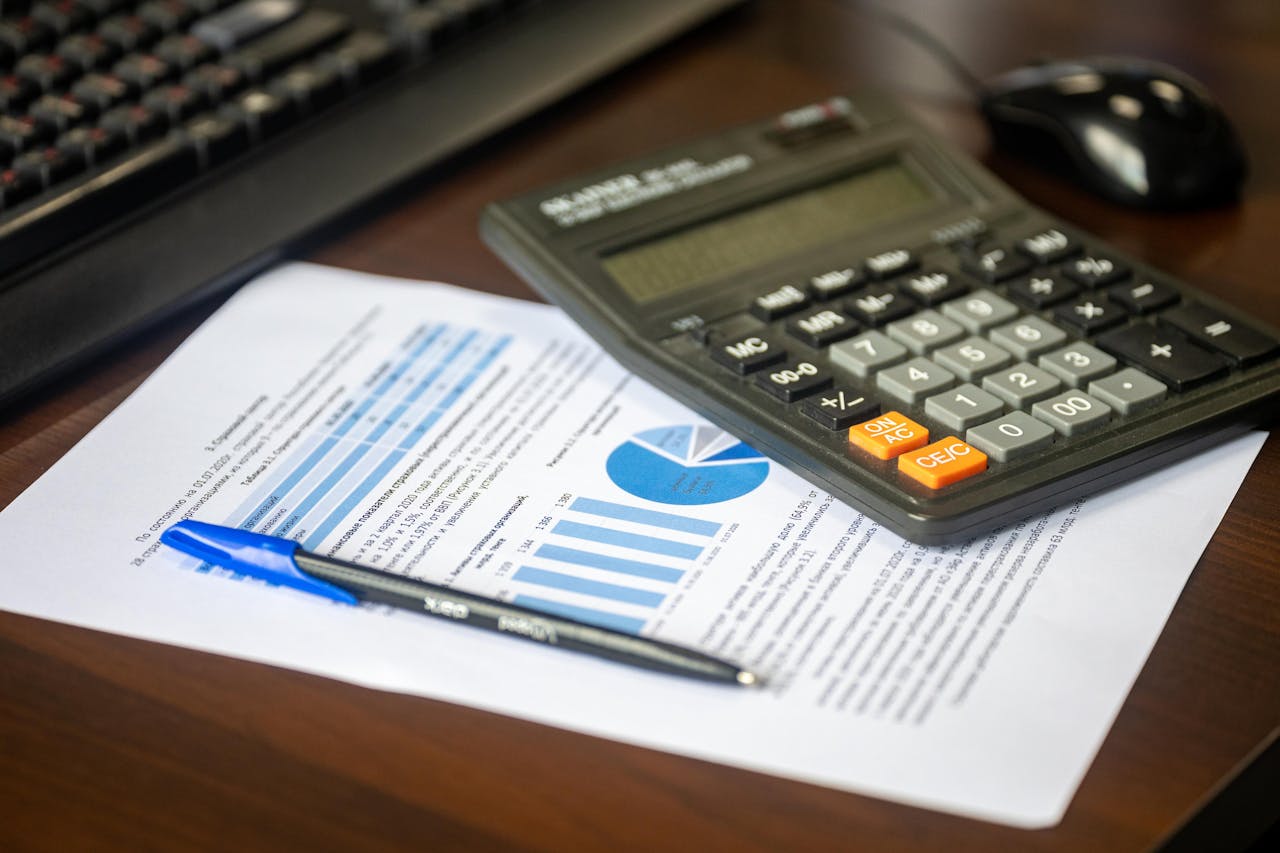 Desk with calculator, financial report, and pen, suggesting business analysis.